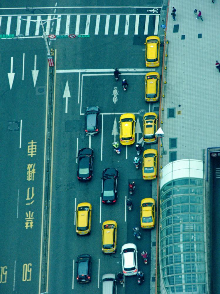 View of a street crossing from above, with many yellow cabs waiting at a red light with some scooters driving in between