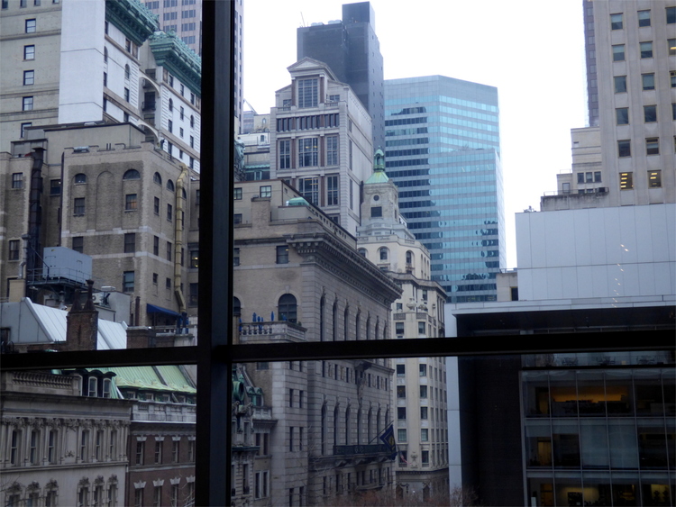 View out of a large window into a narrow street lined by high-rise buildings