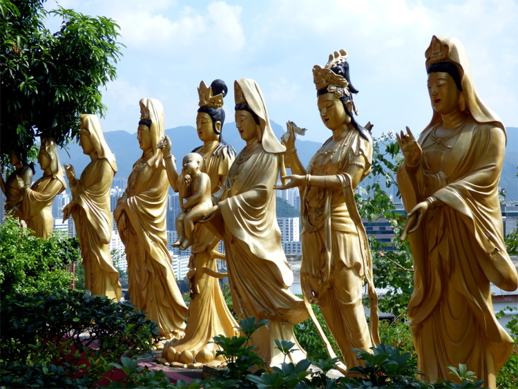 A row of golden life-size statues in various poses standing in a garden
