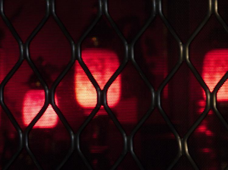 Three glowing red lanterns illuminating a dark room photographed through a metal grate