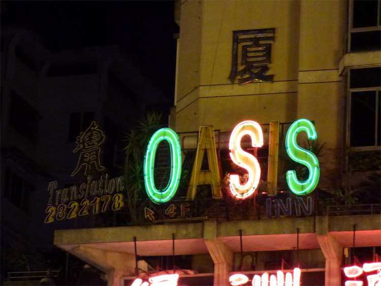 A green and red neon sign reading 'OASIS' with two defective letters on a building at night