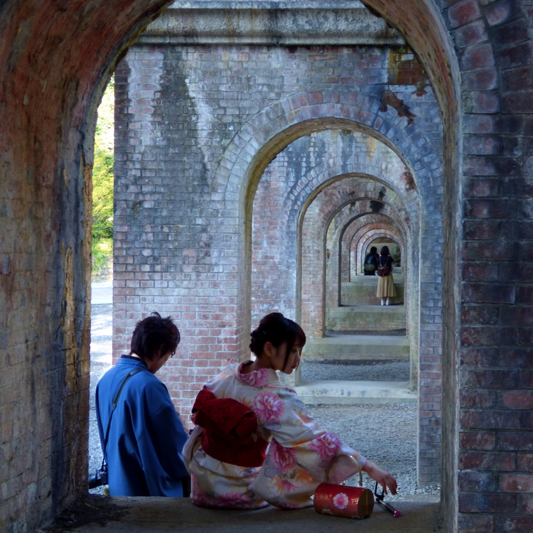 A man and a woman in traditional Japanese clothing sitting in the arch of a red-brick support pillar