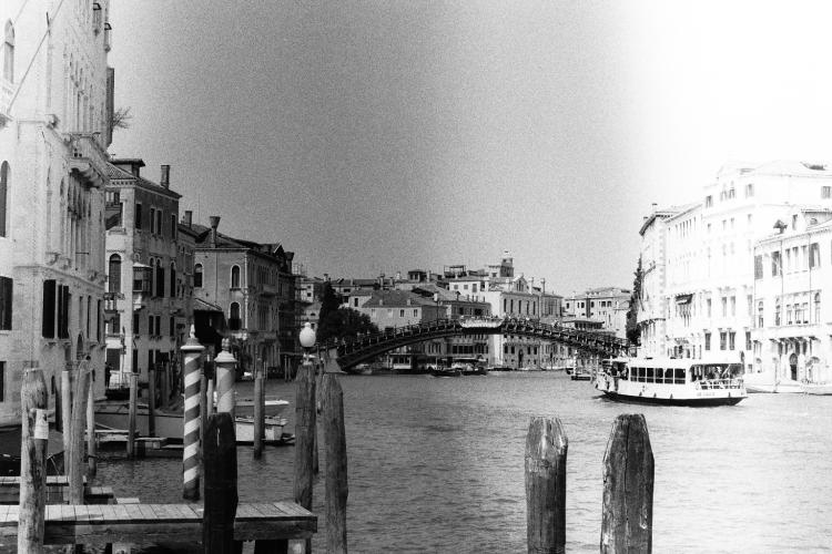 View of an arched bridge over a wide canal with houses to either side, with a boat passing by