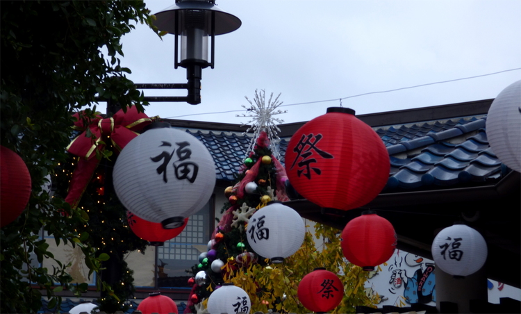 Red and white lanterns with Chinese characters hanging among a decorated Christmas tree outside