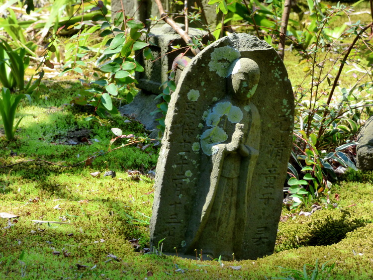 A mossy tombstone-like stone showing a person in prayer appearing to sink into the grassy ground