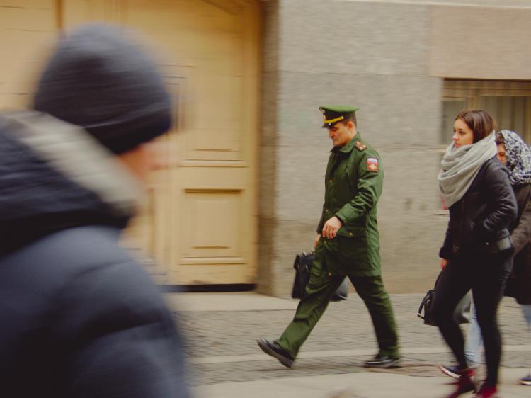 A man in a green police uniform walking across a public square