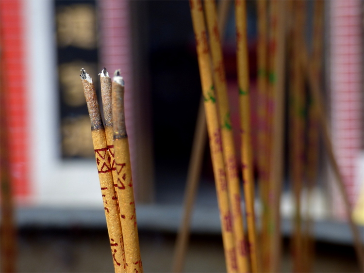 Close-up of three burning sticks of incense with red ornaments and more incense in the background