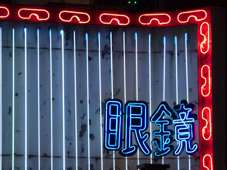 Close-up of a red, blue and white neon sign at night, showing the Chinese characters for 'glasses' surrounded by a border of stylized glasses