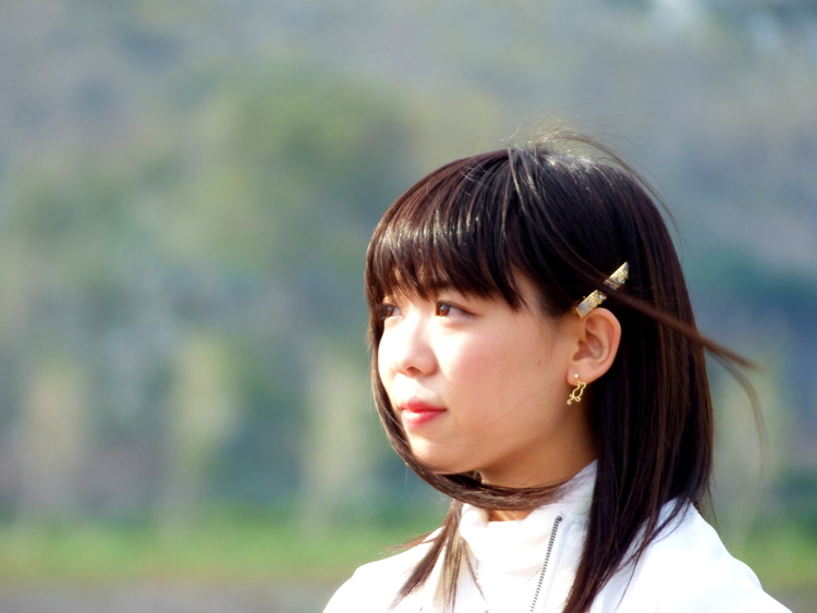 A woman with a golden cat-shaped earring looking off into the distance, her dark brown hair flying in the breeze