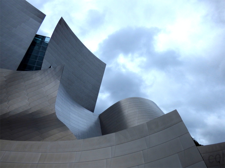 A building made of abstract, wave-like metal surfaces against a cloudy sky