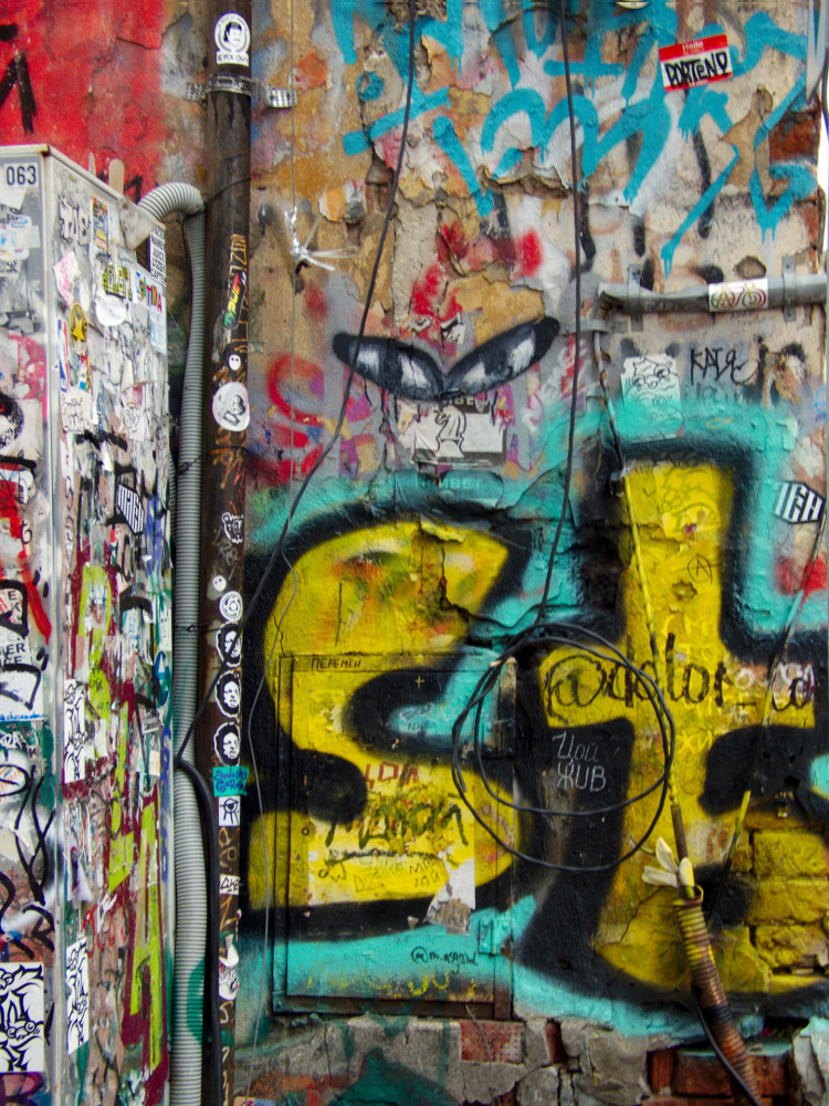 A wall covered in graffiti tags and stickers, with yellow and black spray-painted letters reading 'st'