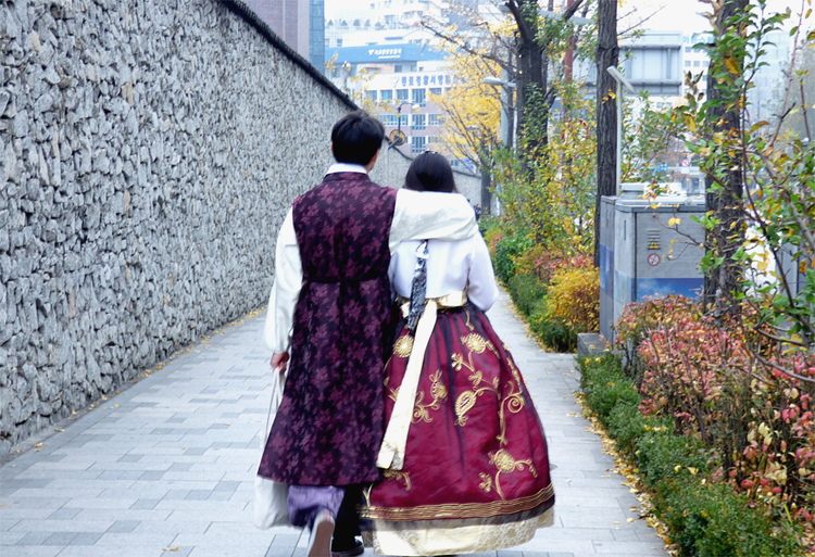 A man and a woman in traditional Korean clothing walking down a side walk arm-in-arm