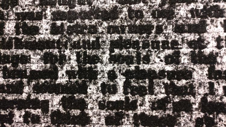 Close-up view of an artwork consisting of a white background on which black particles have been deposited to form text reminiscent of a book page. Most of the words are nearly illegible due to dust and residual particles. The words 'pleasure', 'feel' and 'souls' stand out as being among the more legible.