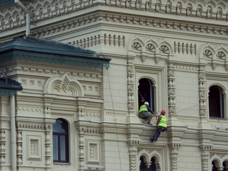 Two workers in high-viz vests descending from a window in a highly decorated, sandstone-coloured facade
