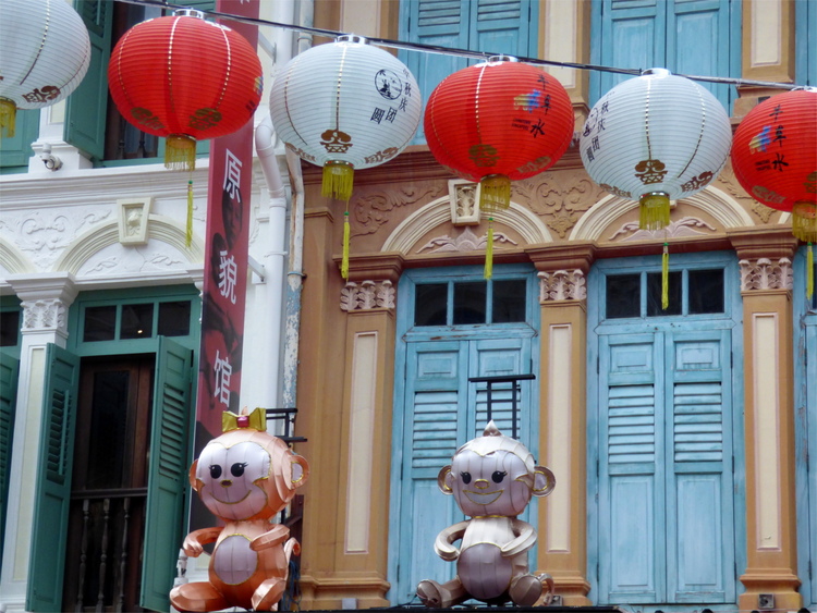 Two small monkey sculptures sitting in front of colonial-style facades under white and red lanterns