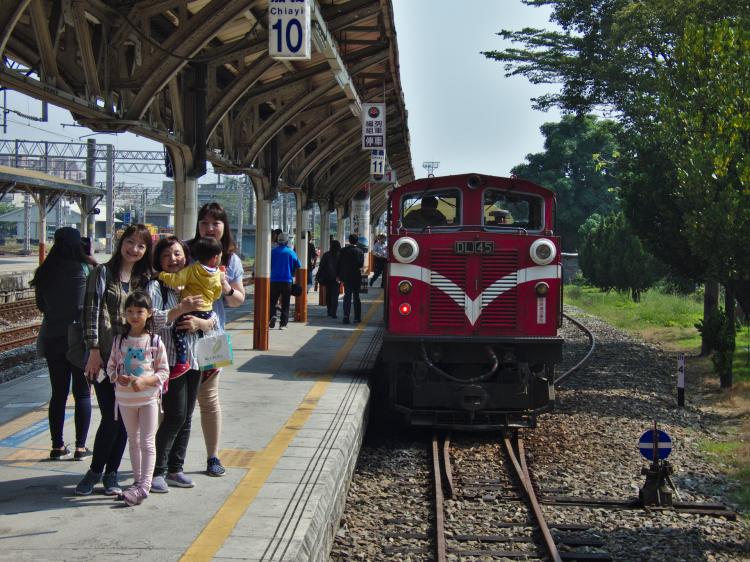 A family happily posing for a group picture next to a red vintage train in a train station