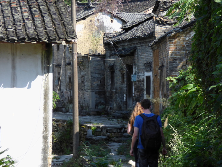 Jan and Katha walking away from the camera on a narrow path through a Chinese village