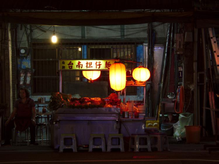 A small street food stall on the side of a street at night, illuminated by three red lanterns