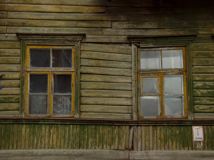 Two windows in a crooked, faded green wooden facade