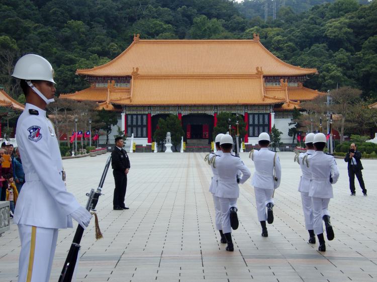 Soldiers in ceremonial white uniforms marching towards a shrine