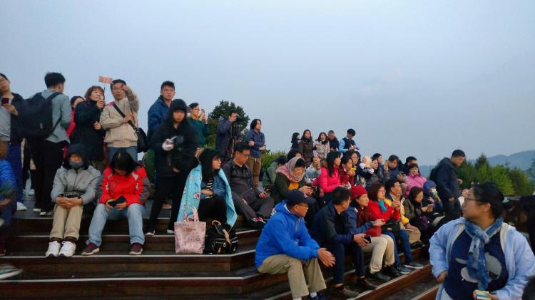 A crowd of Asian tourists sitting on a multi-tiered podium 