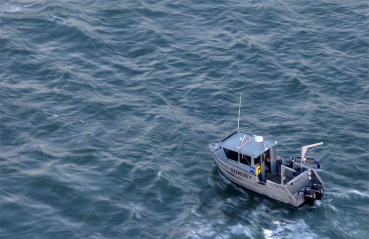 A small grey surveying boat driving through rough waters