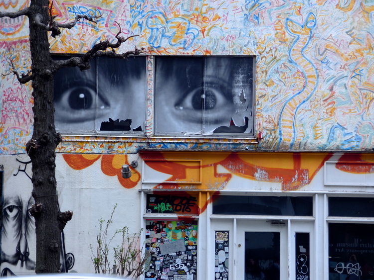 Street-art on the facade of a building showing a black-and-white picture of wide-open eyes and colourful doodles around it