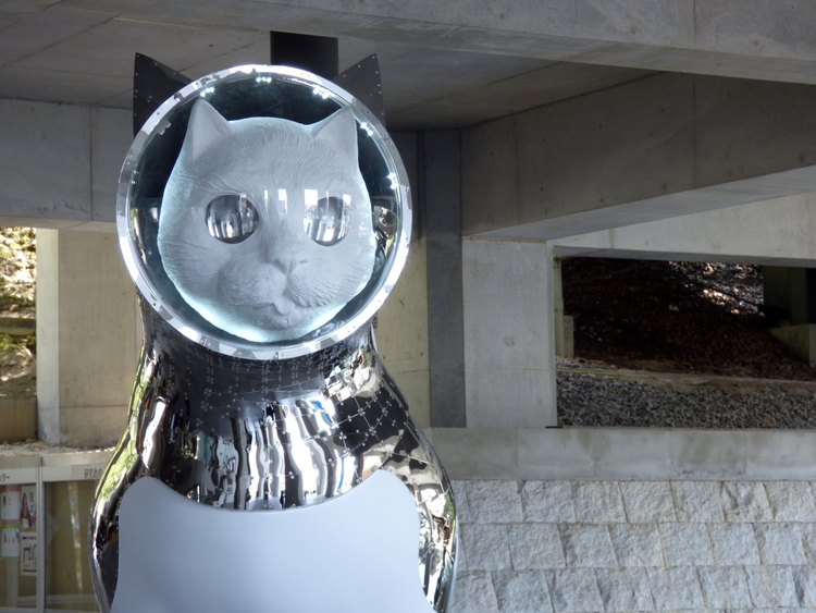A sculpture of a large white cat wearing a metallic space suit and a glass sphere on its head