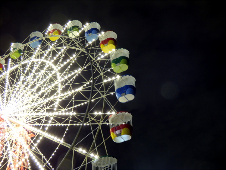 An empty, white Ferris wheel at night with multi-coloured cabins and white lights along the spokes