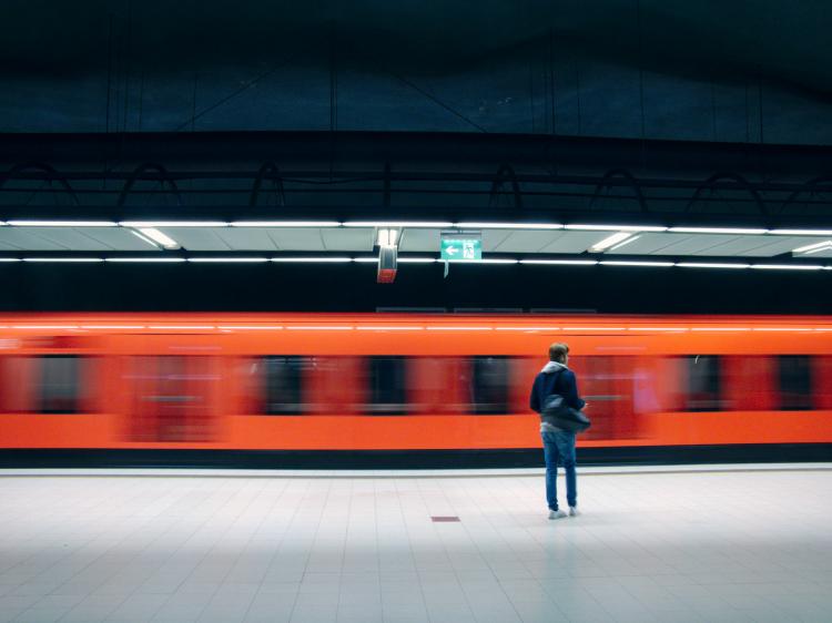 A man standing in front of a bright orange arriving train in an underground metro station