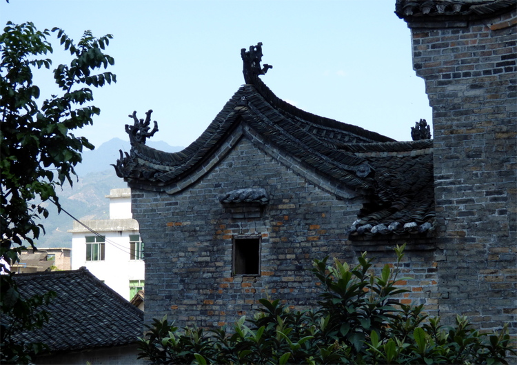 An old, grey-brown brick building with a single small window and an arched tile roof with Chinese-style decorations