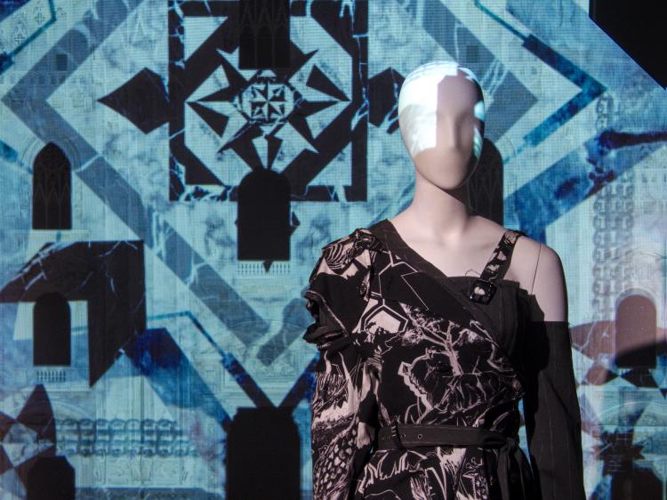 A mannequin in a patterned black-and-white dress standing in front of a projected blue-and-black background