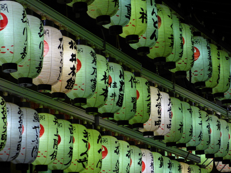 Rows of glowing paper lanterns in various shades of green with black Japanese writing