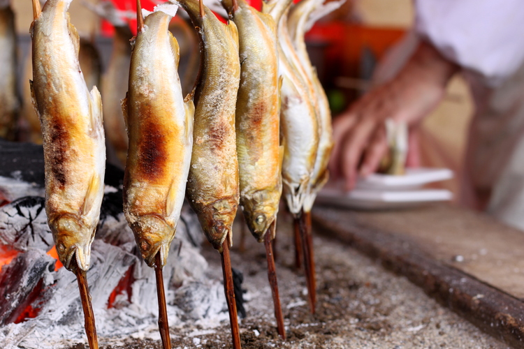 Small fish skewered whole and arranged in a circle around a small fire to cook