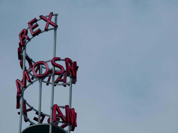 Red neon letters reading 'Amos Rex' forming a spiral in front of a grey sky