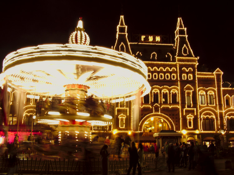 A brightly lit carousel spinning in front of a large building outlined in lights 