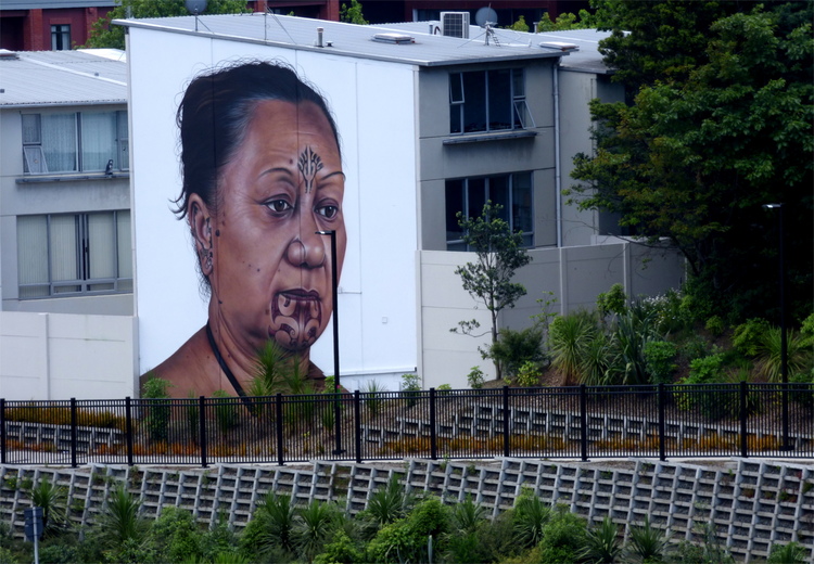 A mural on the side of a white residential building showing the head of a Maori woman with traditional facial tattoos