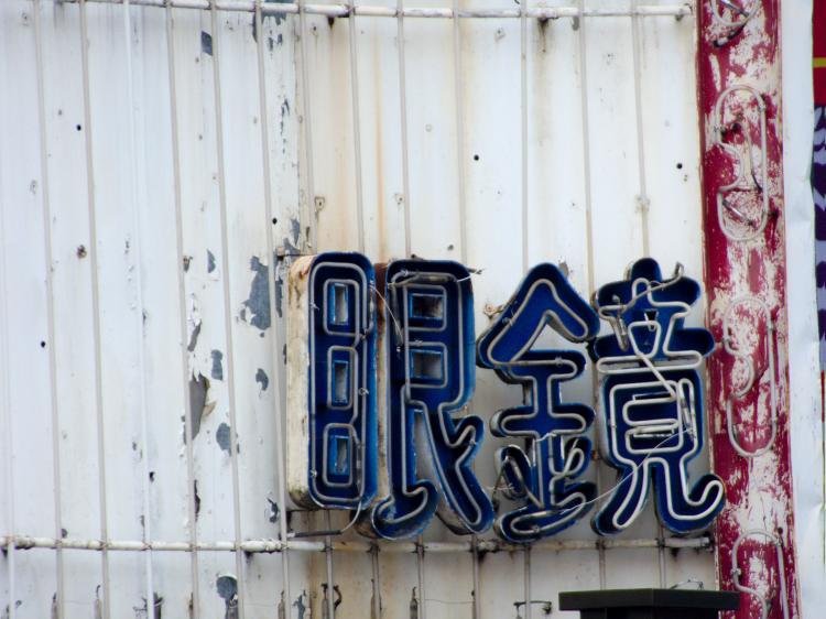 Two crooked blue neon signs of Chinese characters on a white corrugated iron wall with paint peeling off in some places
