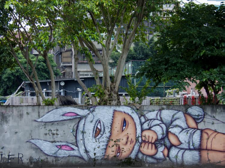 Street-art of a girl in a bunny costume painted on a plain concrete wall with trees in the background