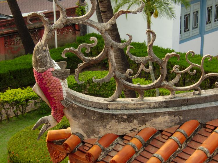 A roof decoration in the shape of a red-scaled fish spewing stylized water onto the shingled roof