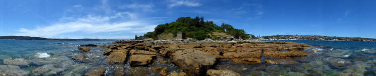 A panorama showing a landscape of orange-red rocks on the seashore, photographed from the water