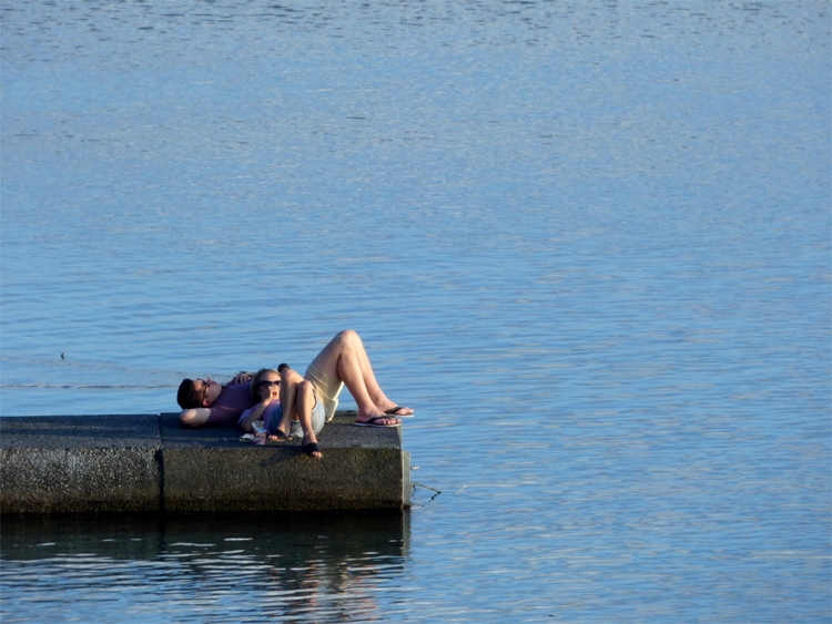 A man and a woman laying on a small concrete pier in a lake enjoying the sun