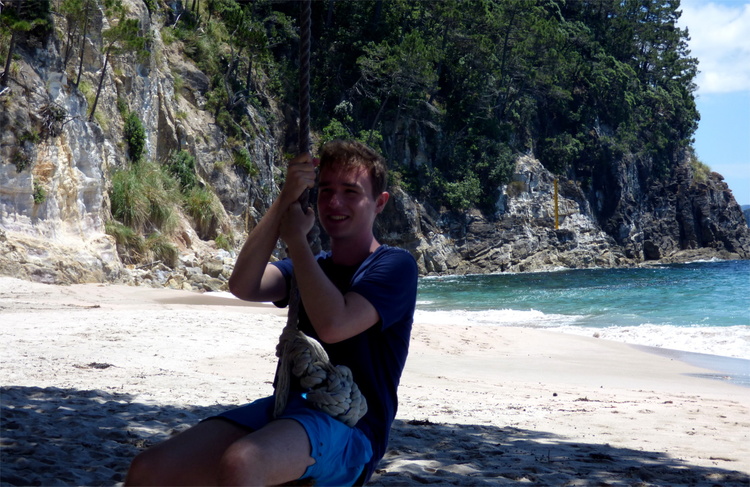 Jan swinging on a rope-swing on a sand beach with rock cliffs in the background