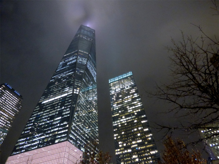 A look up the One World Trade Center and surrounding skyscrapers piercing through the fog at night