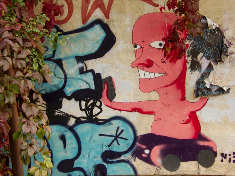Street-art on a house wall showing a vaguely humanoid pink creature with insane eyes and a huge nose