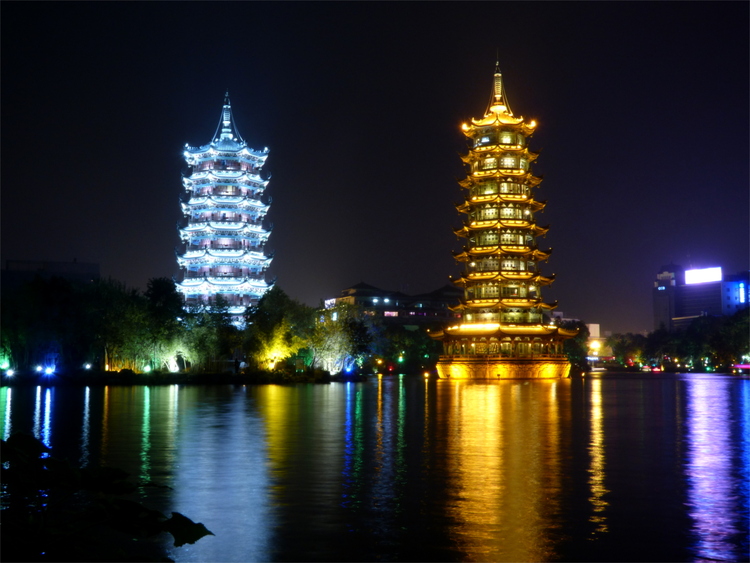 Blue- and orange lit Chinese pagodas and their blurred reflections in a lake at night