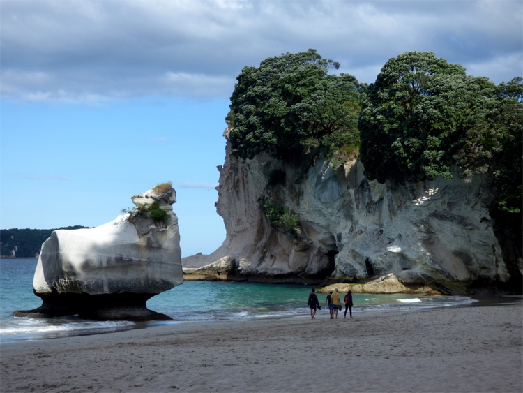 White cliffs and rock formations on the shore with some people walking along the beach
