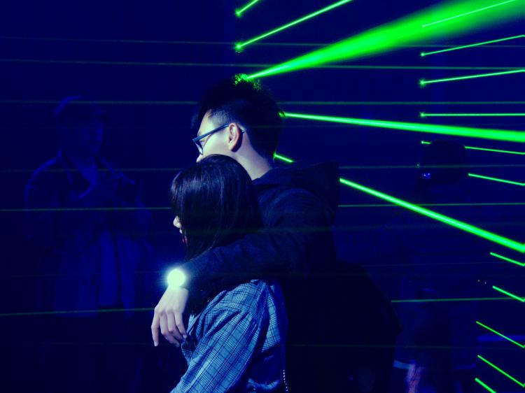 A young couple posing for pictures in a dark, blue-ish room with strong green laser beams forming a wall behind them