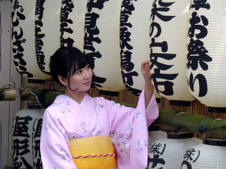 A woman in a light pink Kimono posing for pictures in front of white paper lanterns