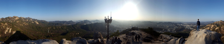 Panorama showing a smooth, rocky mountaintop with some people and a cellphone tower in the center